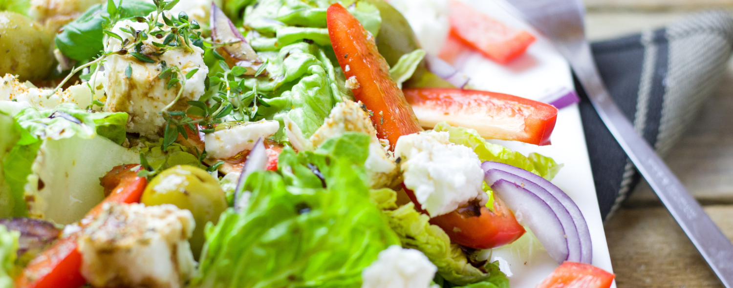 Fresh Greek salad with feta cheese, tomatoes, cucumbers, and olives drizzled with olive oil and garnished with herbs.