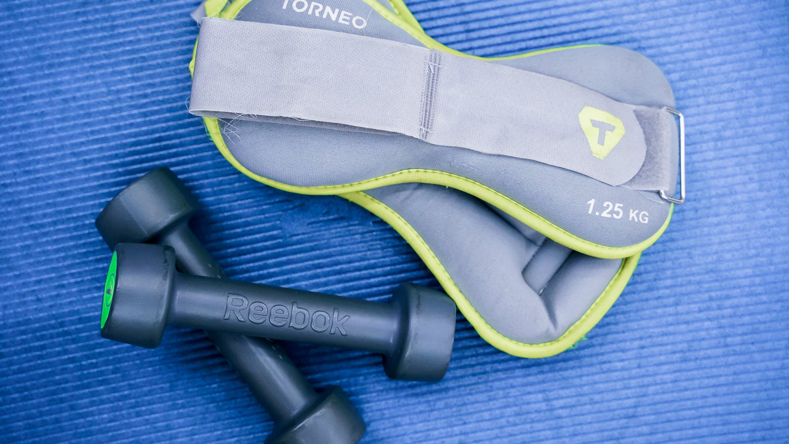 Dumbbells and ankle weights arranged on a blue exercise mat.