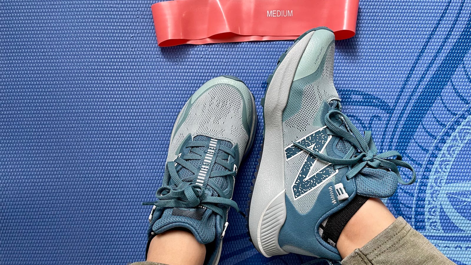 Athletic shoes and a resistance band on a blue exercise mat.